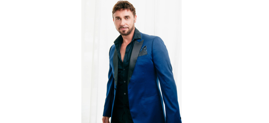 Nathan Foley smiles at the camera dressed in a blue suit jacked on a white background